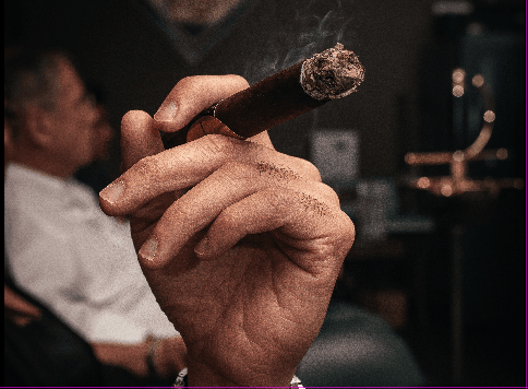 Tobacco in Brazil: Mata Fina, the World's Largest Exporter, and Two Industries in One Country 3 Close-up of a hand holding a lit cigar, with smoke rising.